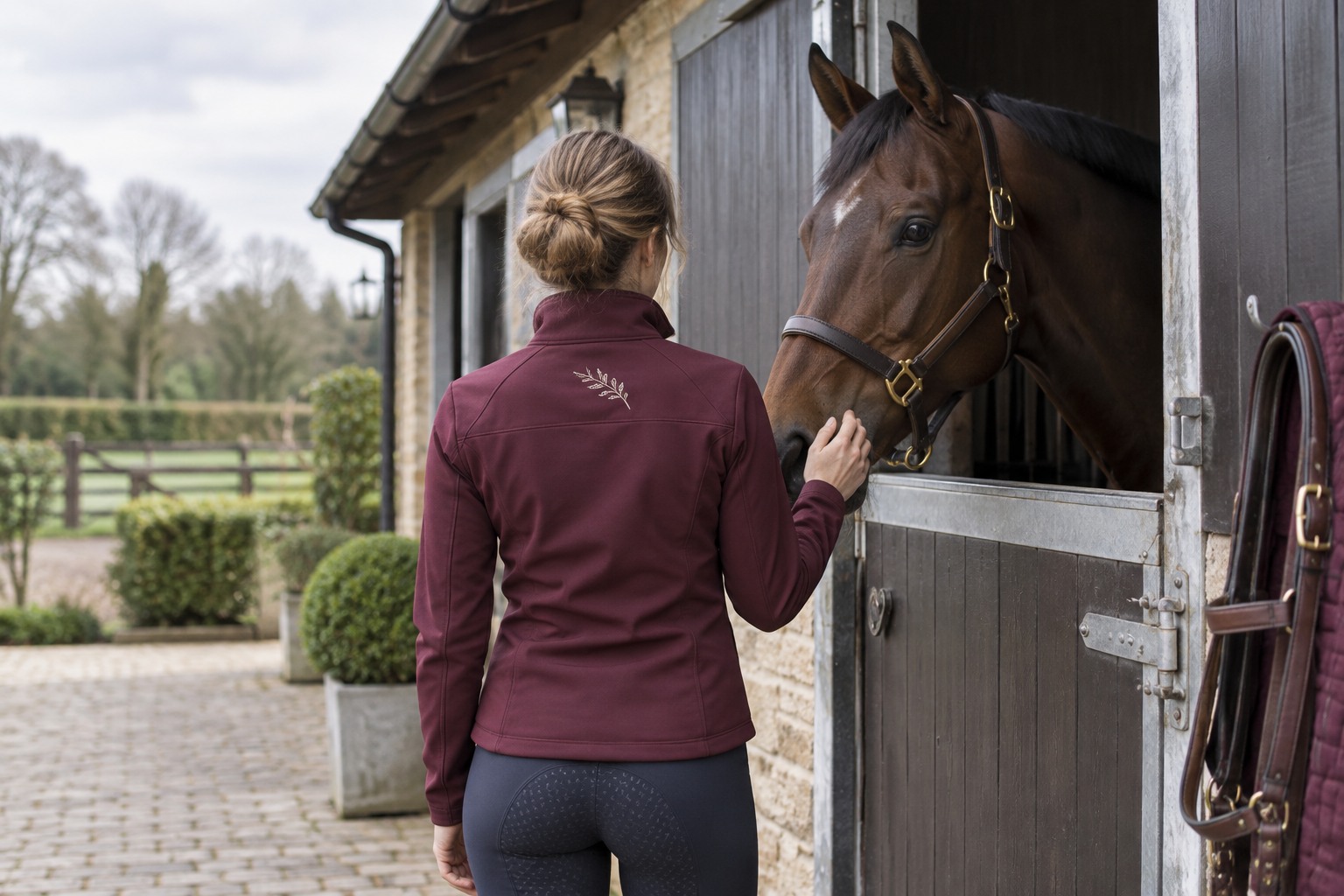An adult equestrian in a burgundy embroidered softshell jacket.