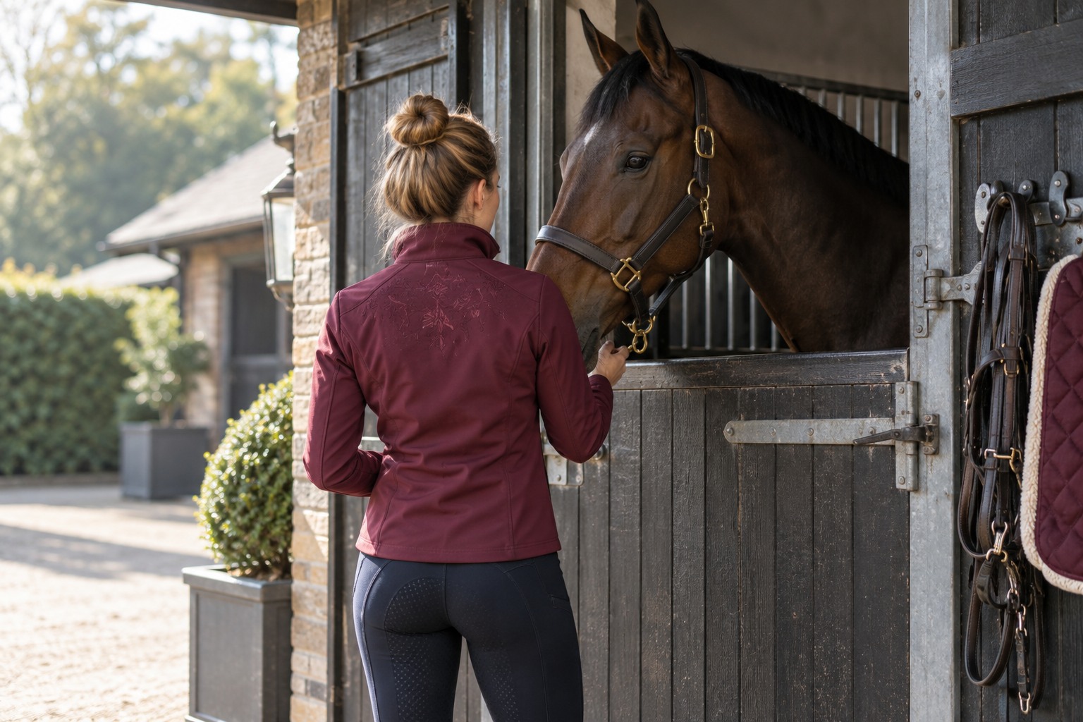 An adult equestrian in a burgundy embroidered softshell jacket.